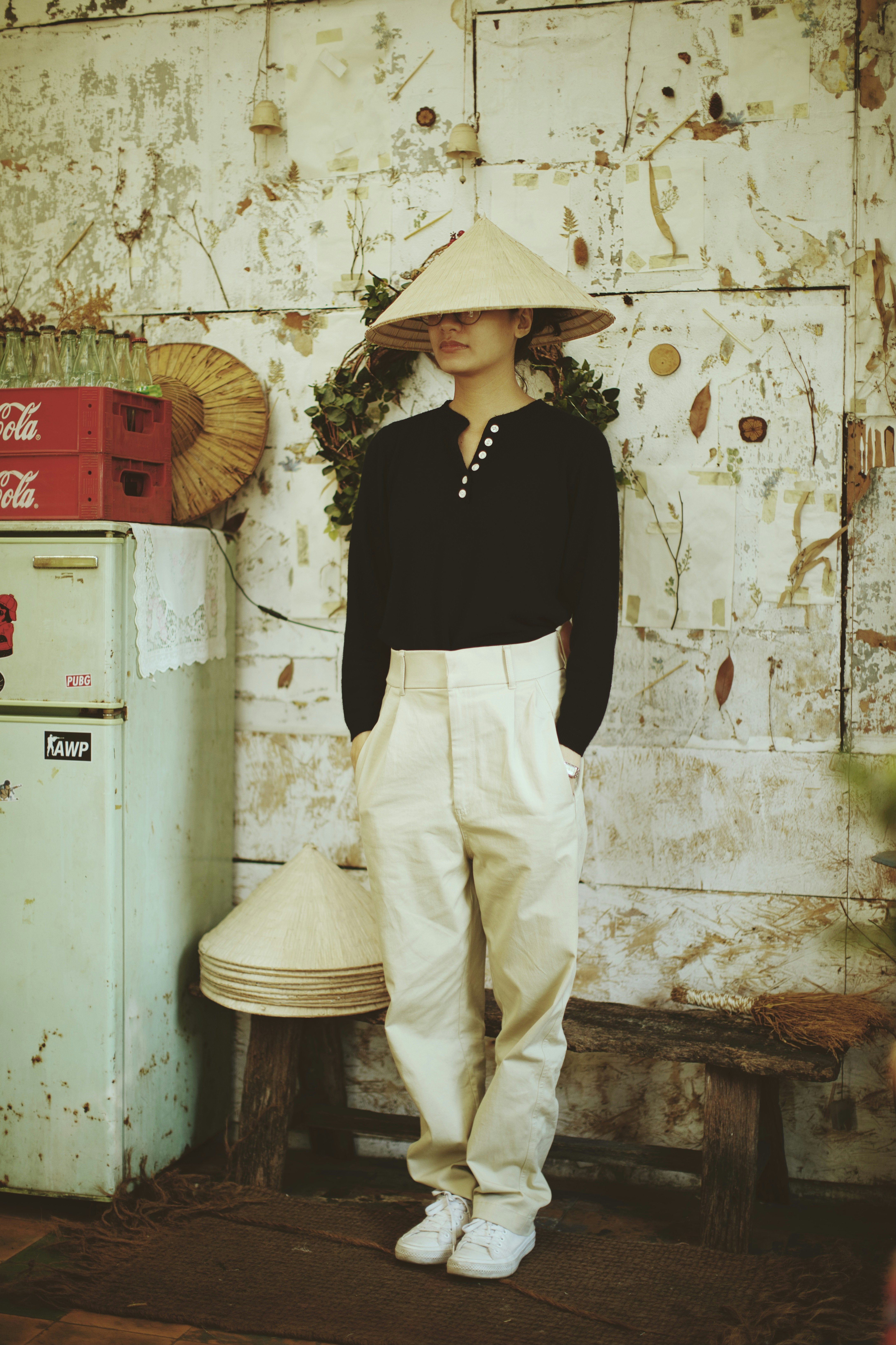 woman in black long sleeve shirt and white pants standing beside white wall